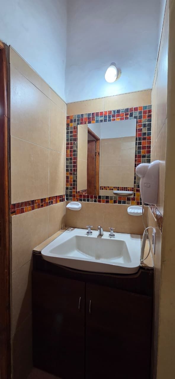 Baño con lavabo blanco, mueble marrón oscuro, espejo y azulejos decorativos.