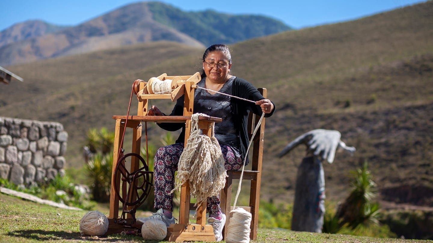 Mujer hilando hilo al aire libre con fondo de montañas.