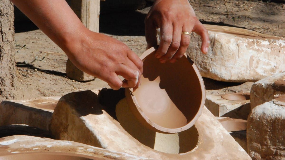 Manos sosteniendo un cuenco de cerámica, colocándolo en un molde. Al aire libre, a plena luz del día.