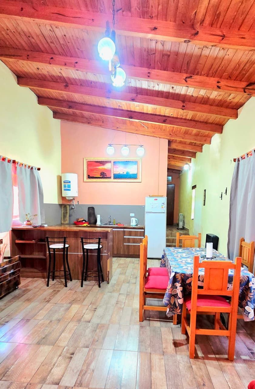 Vista interior de un comedor y cocina rústicos con muebles de madera, barra y techo con vigas a la vista.