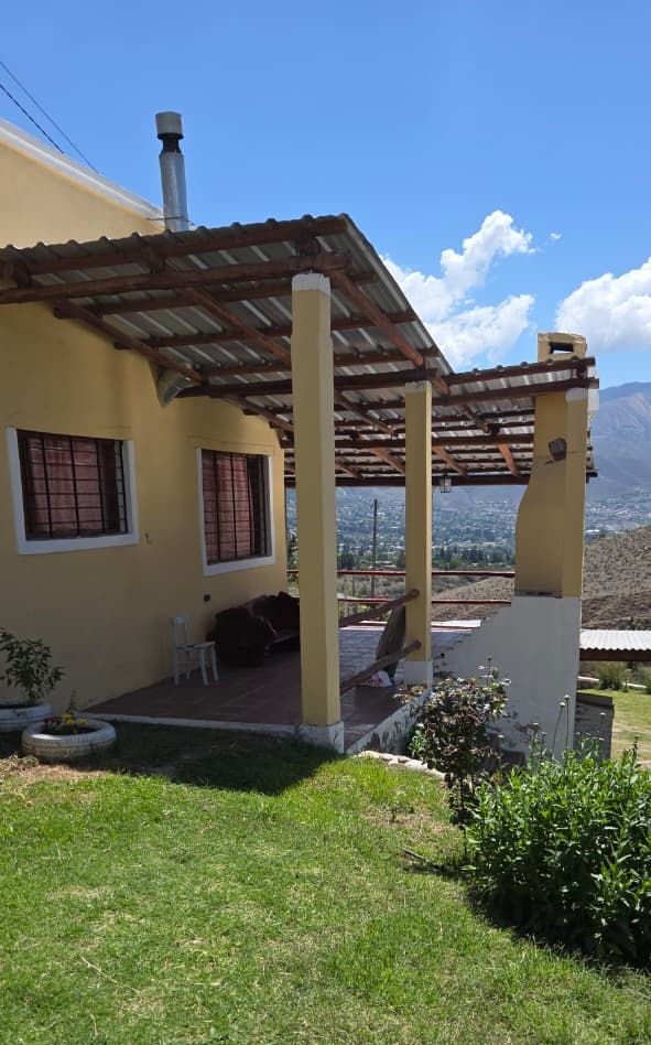 Casa amarilla con un porche cubierto con vistas a un valle bajo un cielo azul brillante.