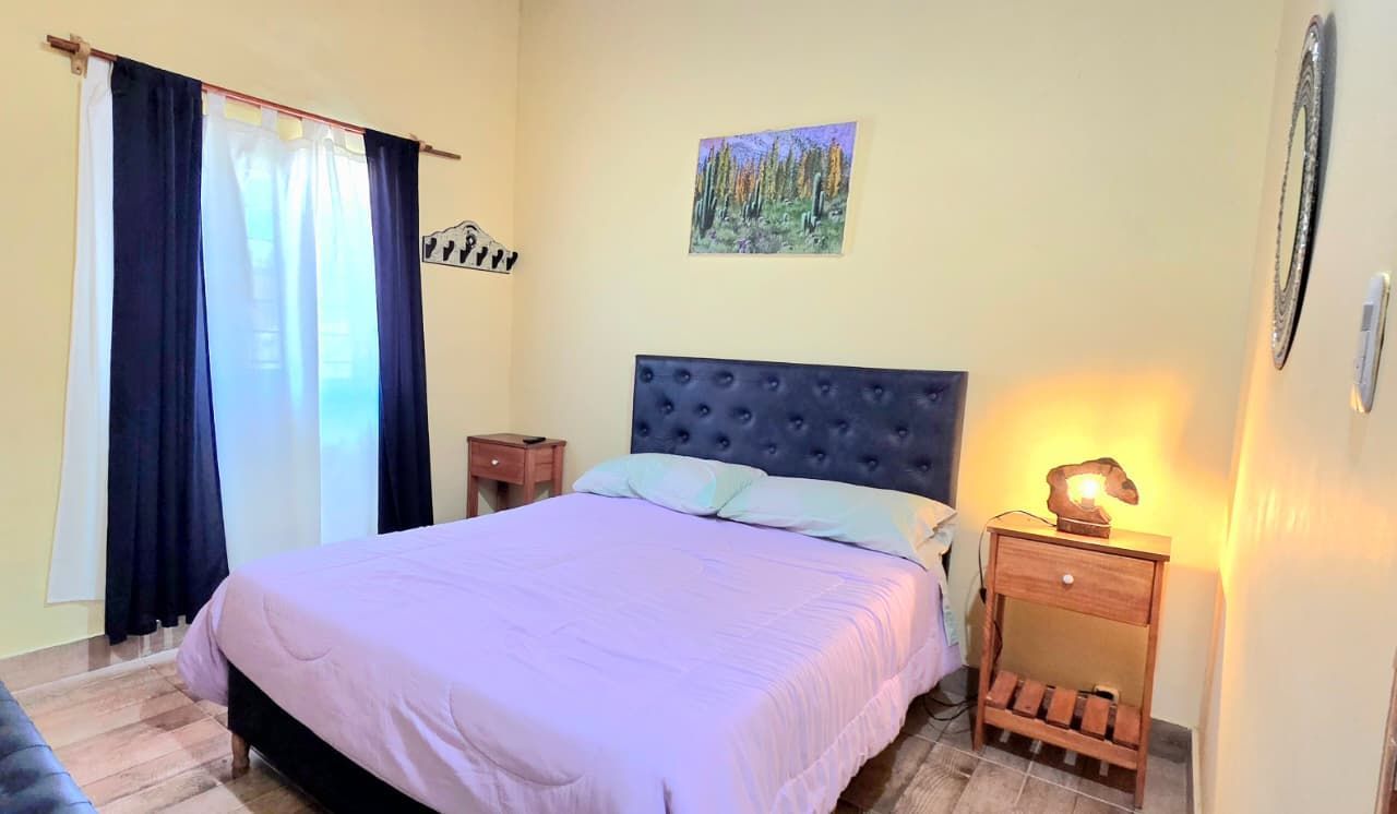 Dormitorio con ropa de cama, mesitas de noche, ventana y arte de pared en color lavanda.