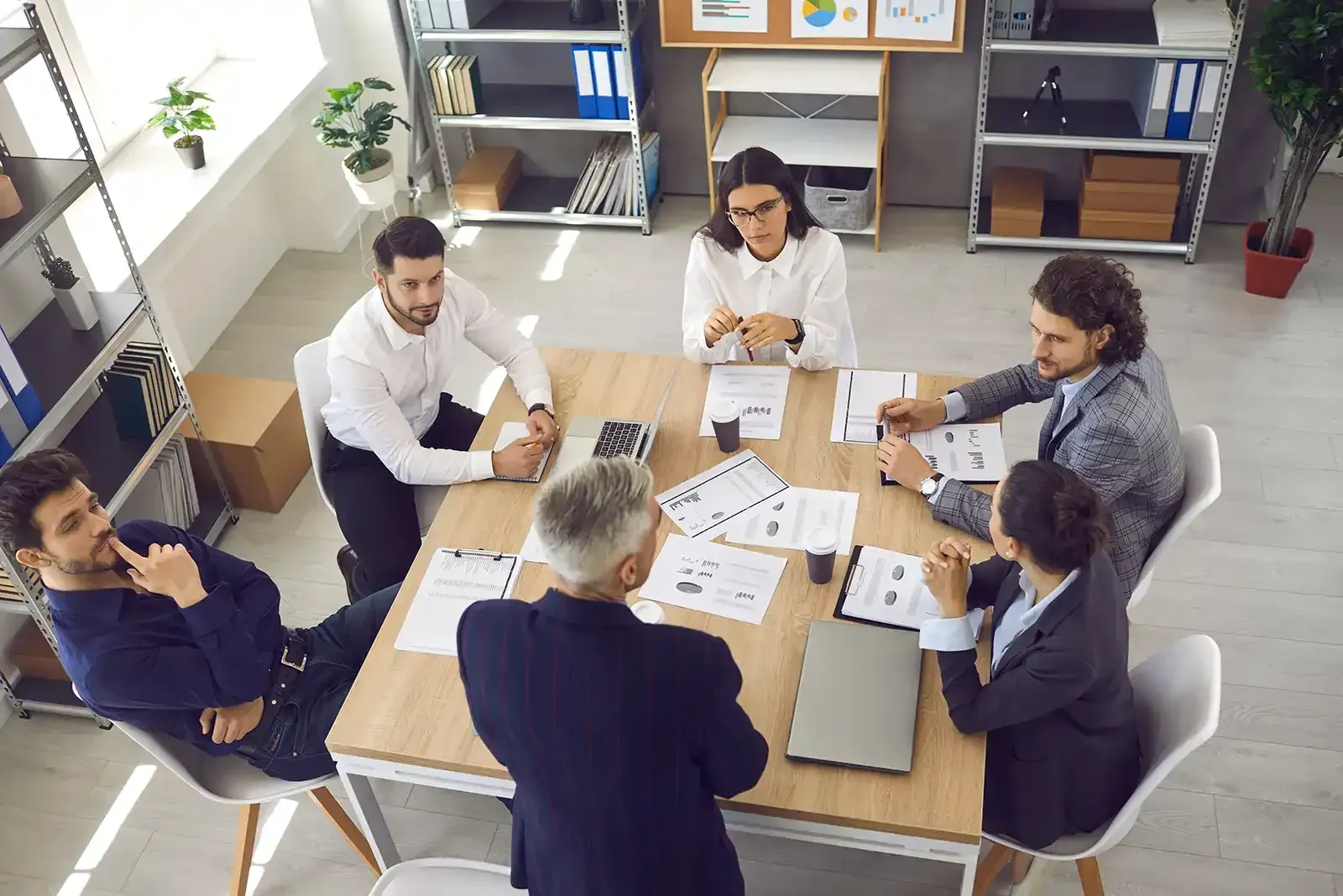 People seated around a wooden table in an office, reviewing documents.