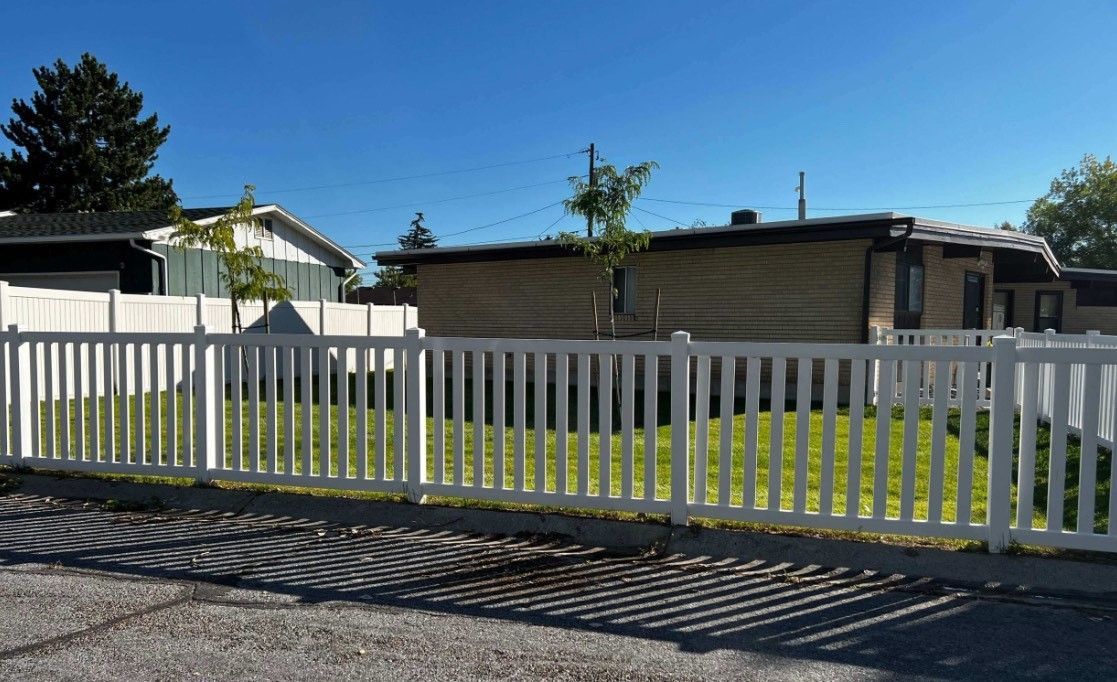 A white fence is surrounded by trees and a stone wall.