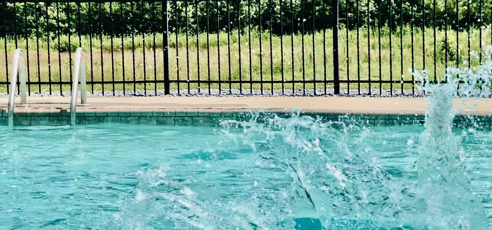 A person is jumping into a swimming pool with a fence in the background.