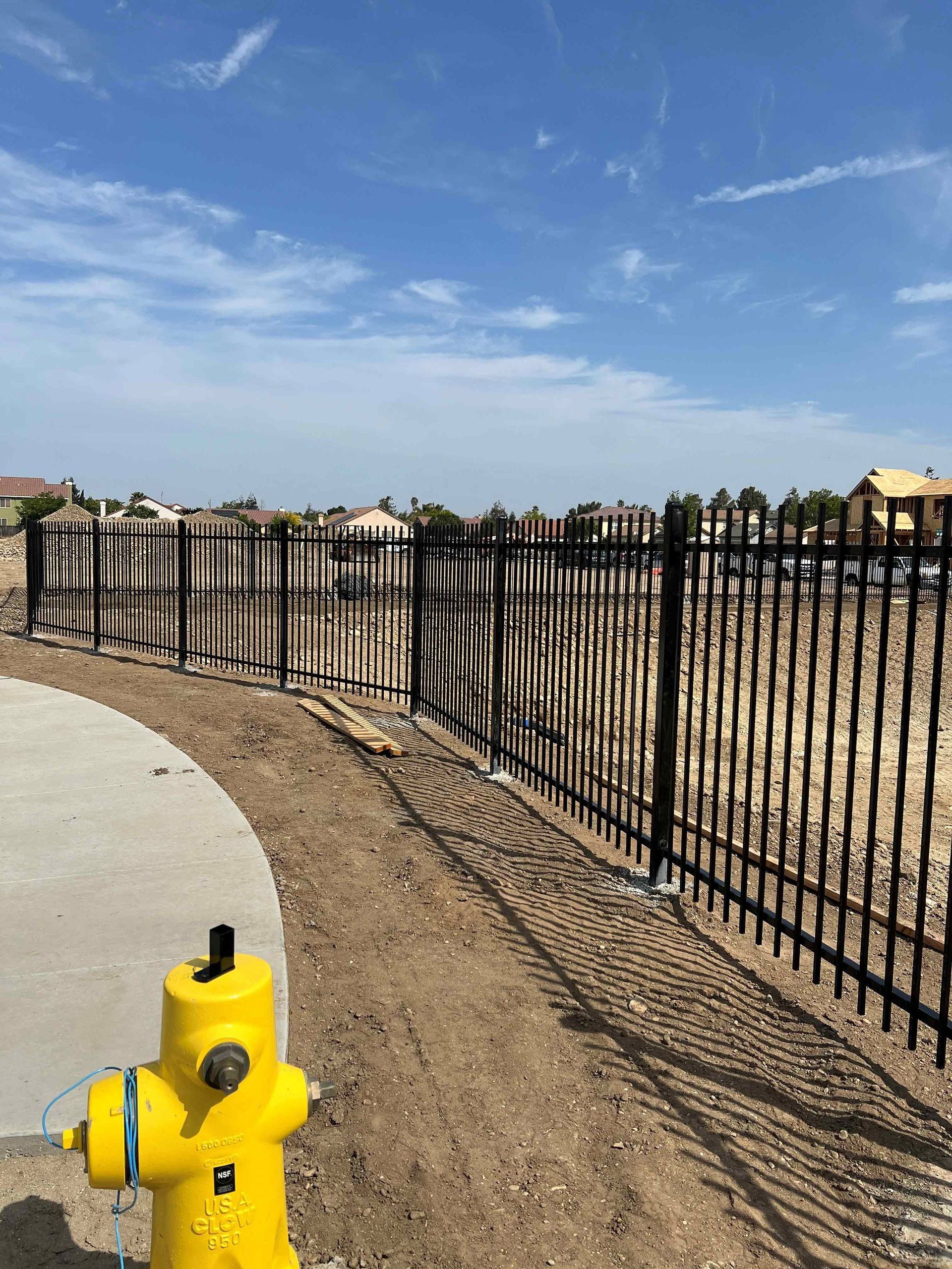 A yellow fire hydrant is sitting next to a black fence.