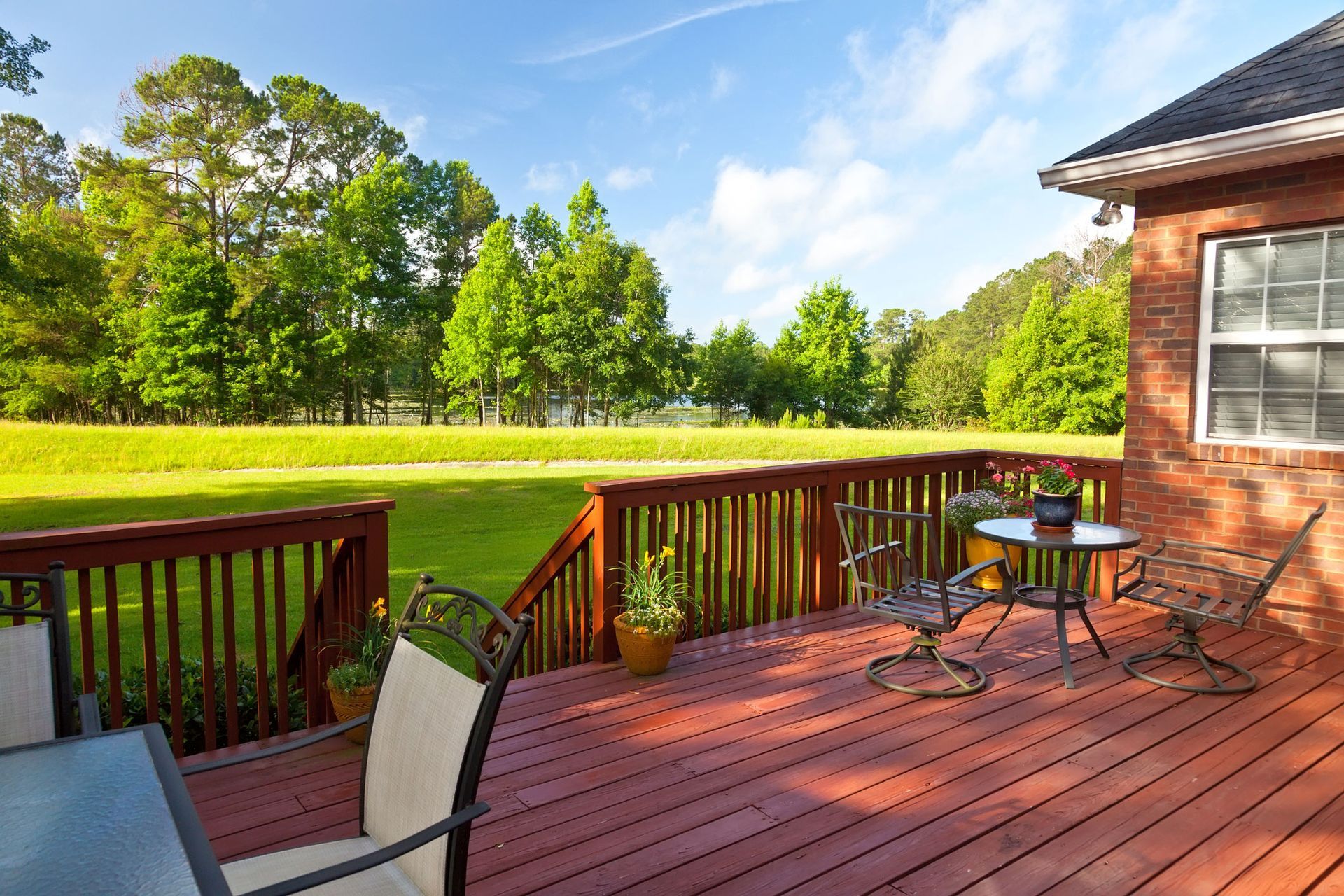 A wooden deck with a table and chairs in front of a brick house.