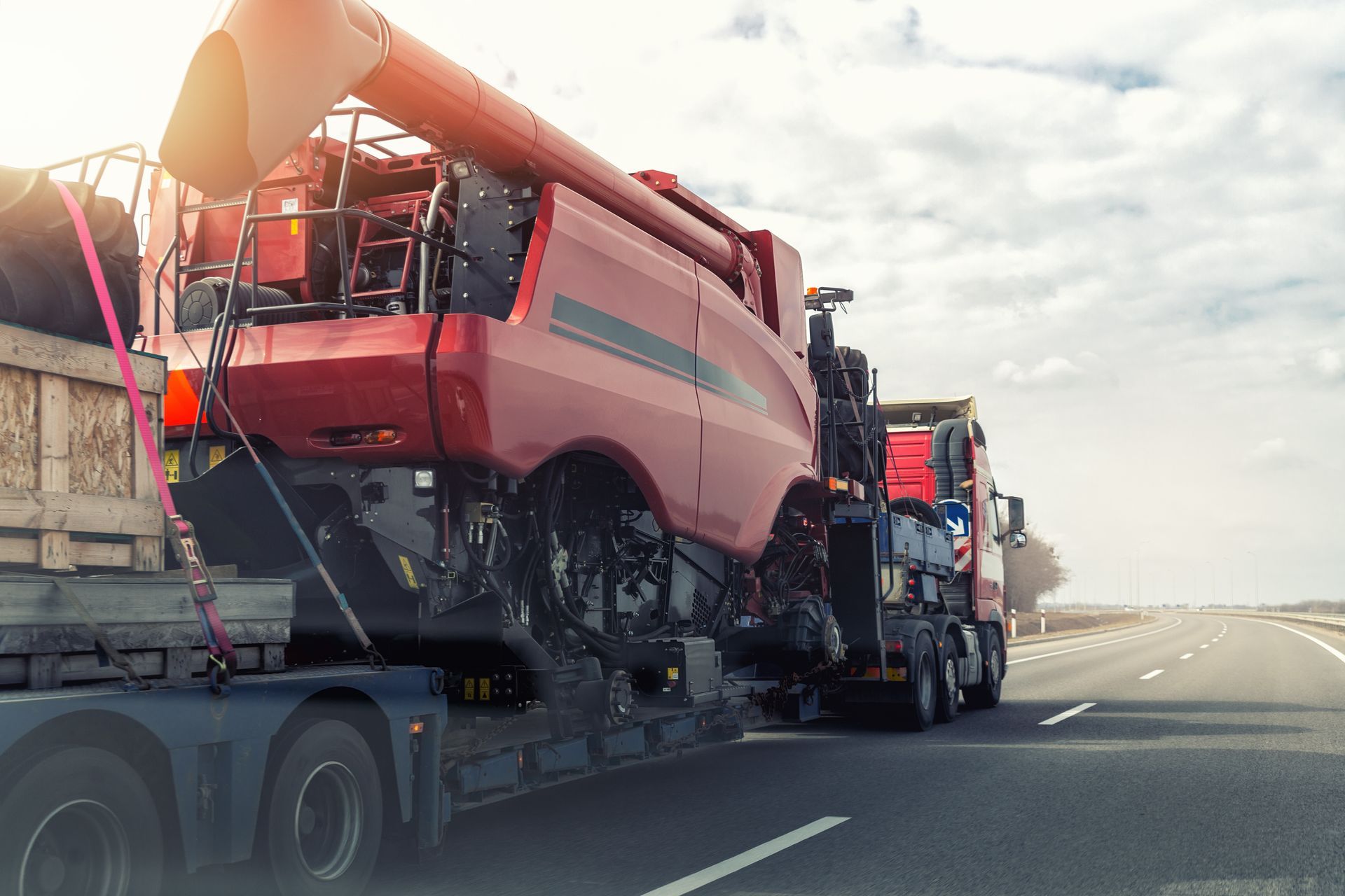 A heavy industrial truck with a semi-trailer platform hauls a machine on a highway road. A heavy industrial truck with a semi-trailer platform hauls a machine on a highway road.