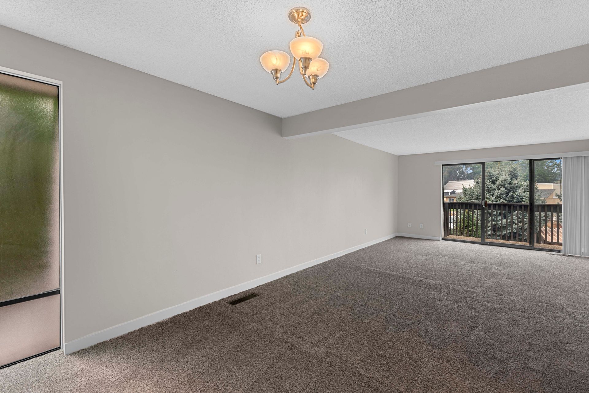 An empty living room with a chandelier and a balcony.