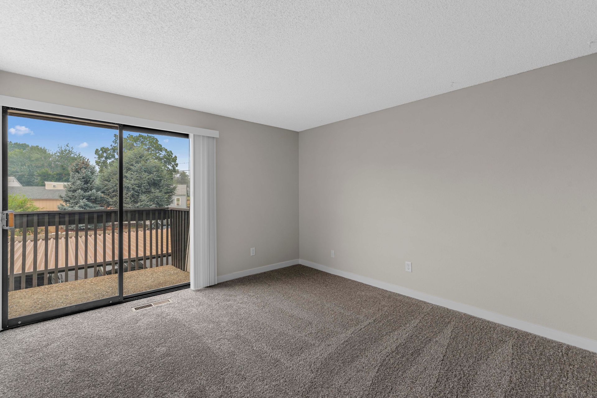 An empty living room with a balcony and sliding glass doors.