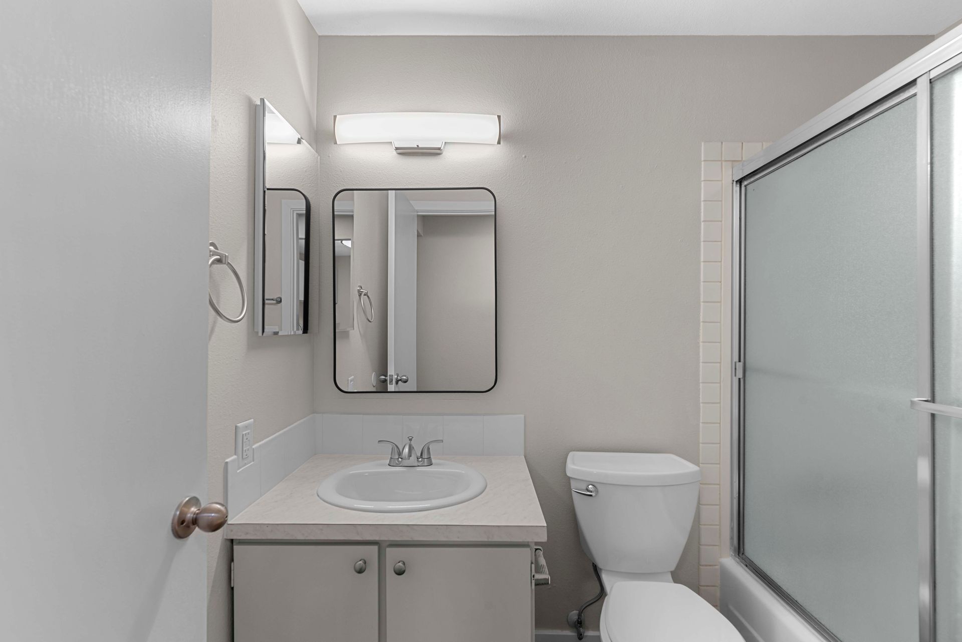 A bathroom with a toilet , sink , mirror and shower.