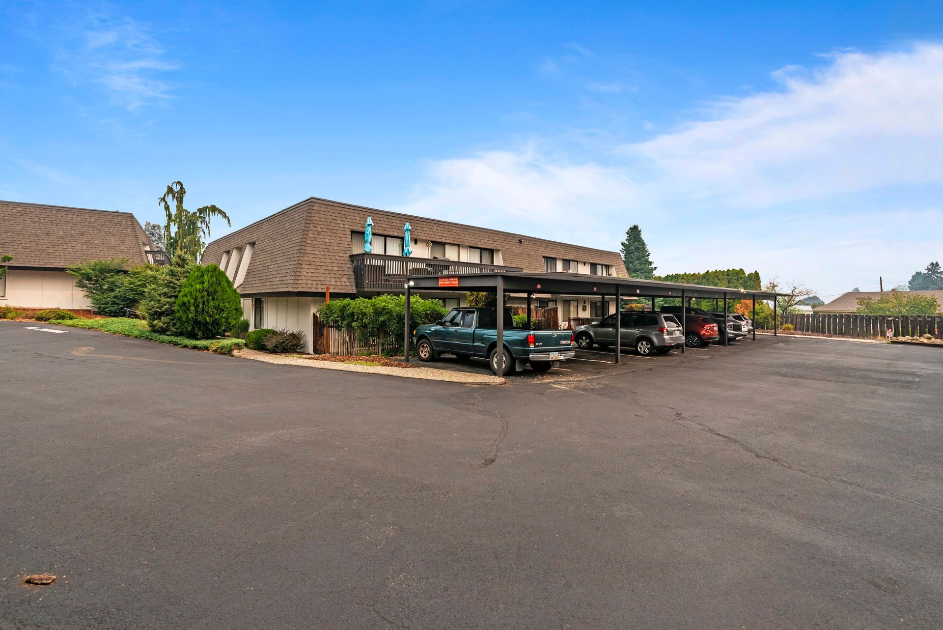 A parking lot with cars parked under a canopy in front of a building.