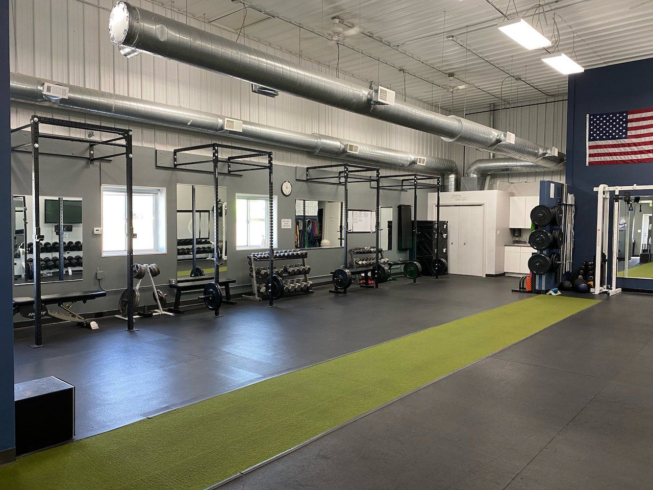 A large gym with a lot of equipment and an american flag on the wall.