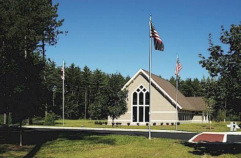 Chapel building with American flags in front, surrounded by trees under a clear blue sky.