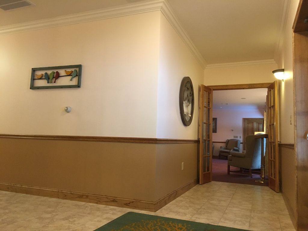Hallway with beige walls, brown wainscoting, and a doorway leading to a seating area.