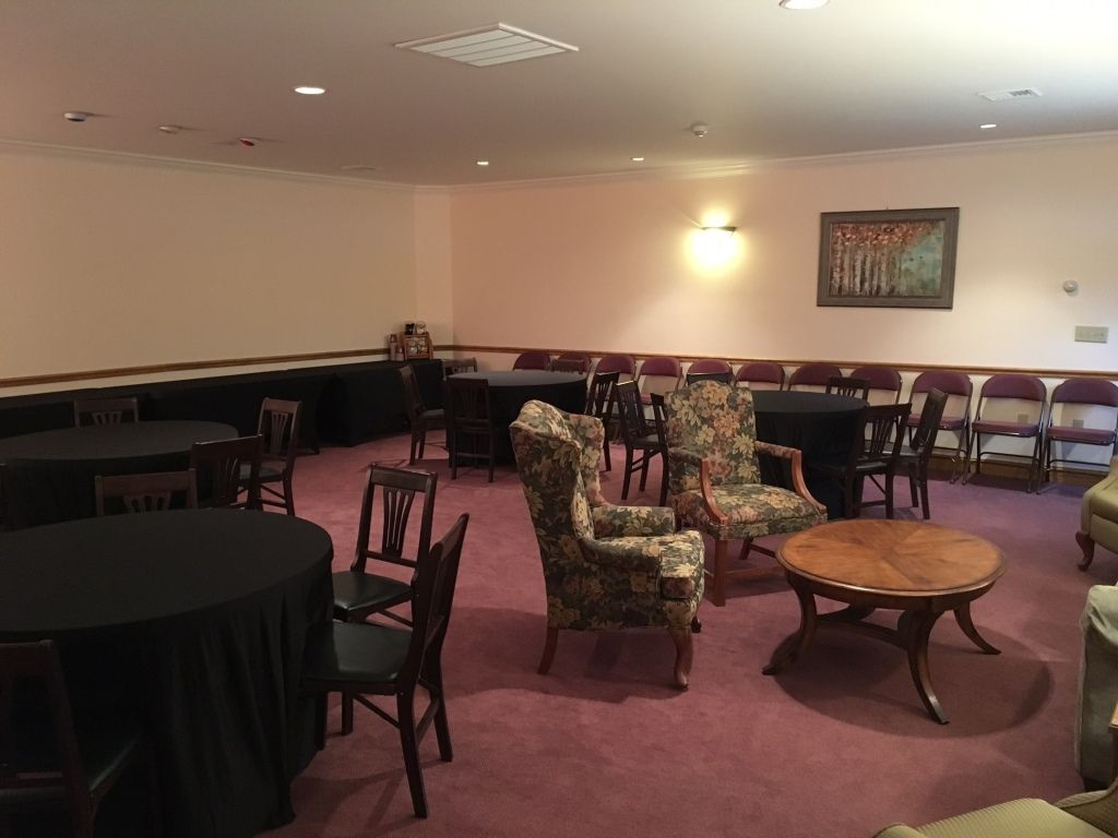 Room with round tables, chairs, and armchairs; a painting hangs on the wall, and the carpet is pink.