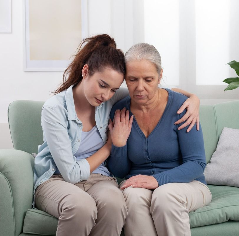 Young woman comforts older woman on a couch.