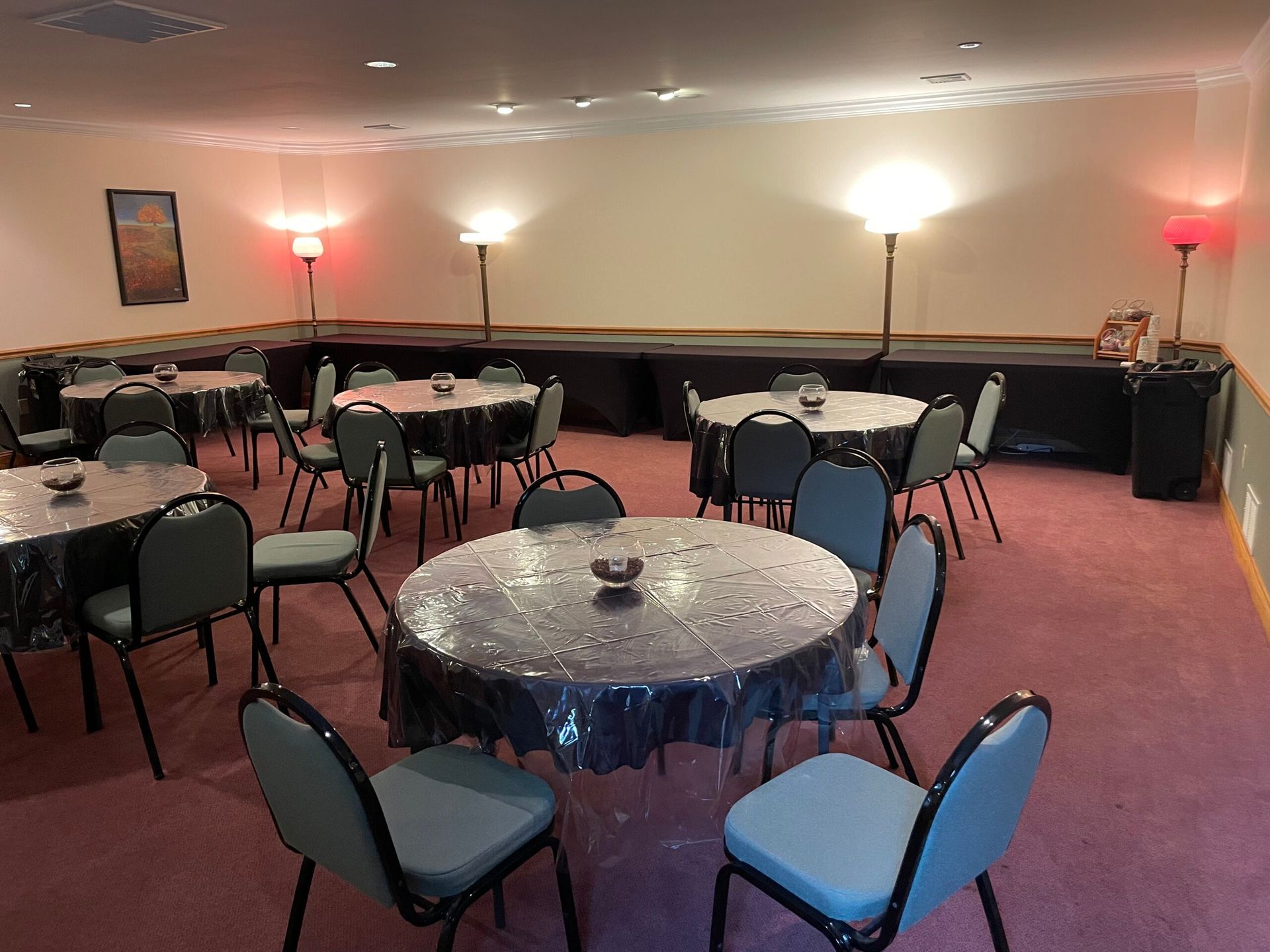 Round tables with black tablecloths and blue chairs in a room with a stage and red and white floor lamps.