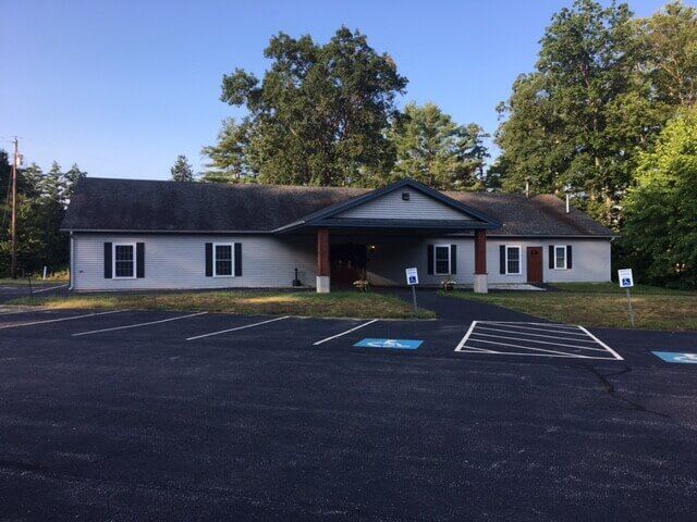 White Victorian-style building with black shutters and a black awning over the entrance, illuminated at night.