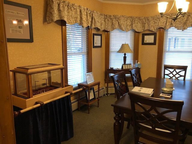 A room with a display case, table and chairs, and a window with blinds.
