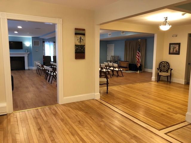 Three rooms with wood floors, doorways, and seating. One room has a fireplace, another an American flag.