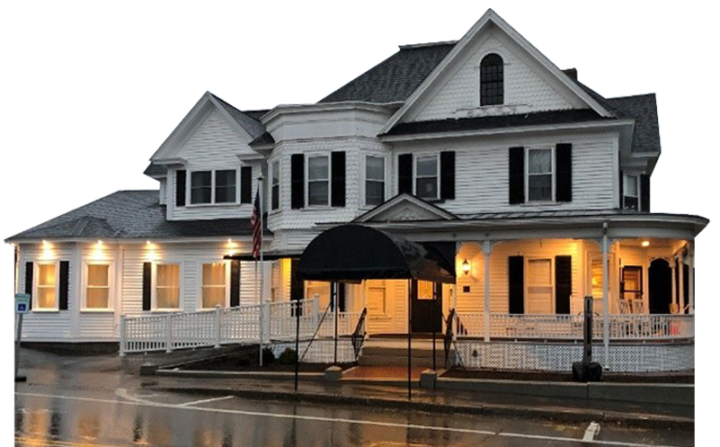 White Victorian-style building with black shutters and a black awning over the entrance, illuminated at night.