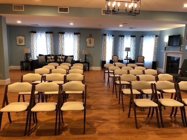 Rows of chairs face a room with windows and a sofa.