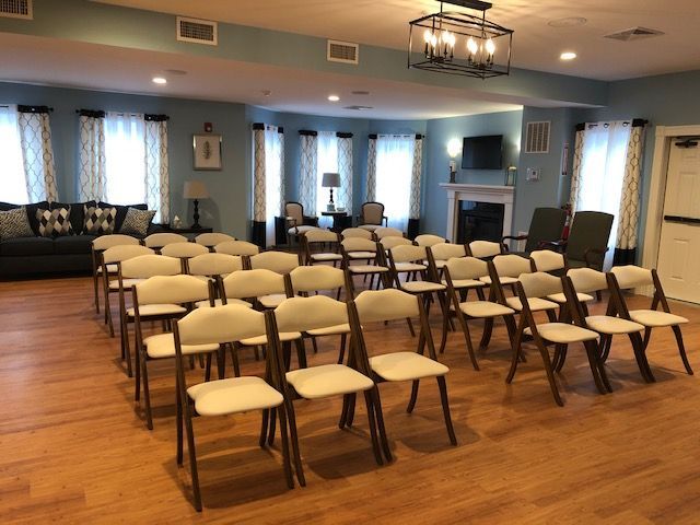 Empty room with rows of chairs, a couch, windows, and a fireplace.