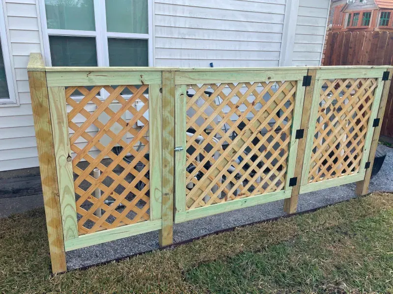 A wooden lattice fence with a gate in front of a house.