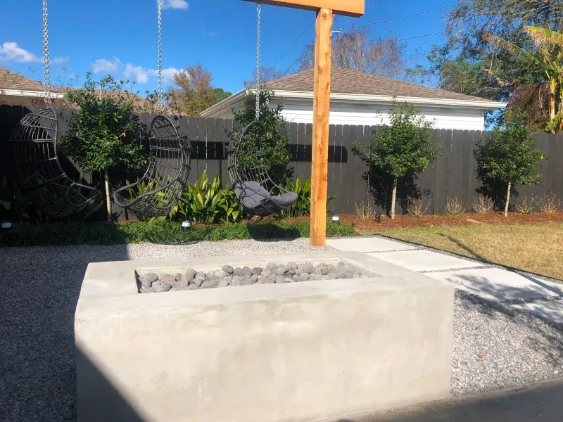 A fire pit in the backyard of a house with a wooden cross in the background.