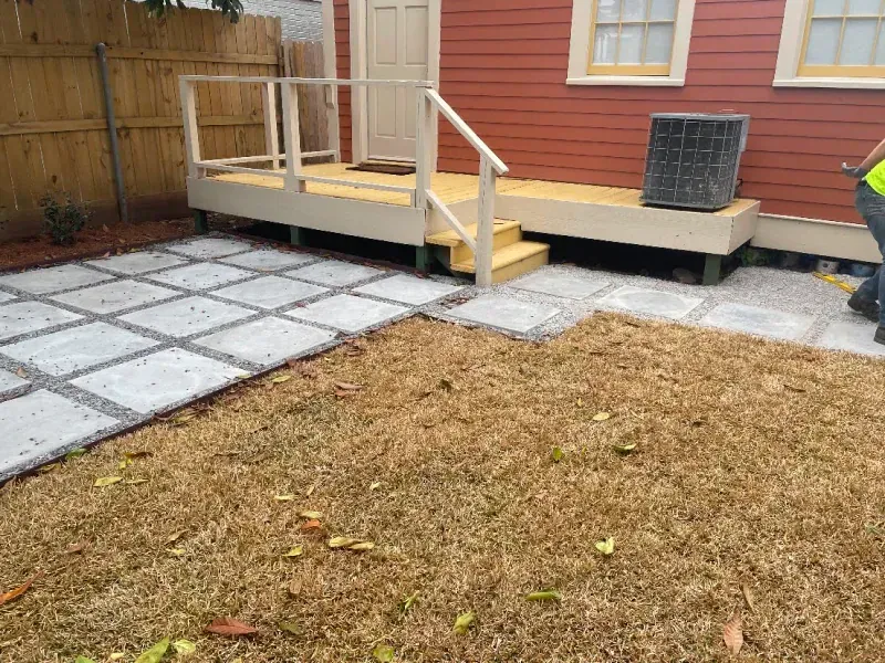 A man is standing in front of a house with a patio and stairs.