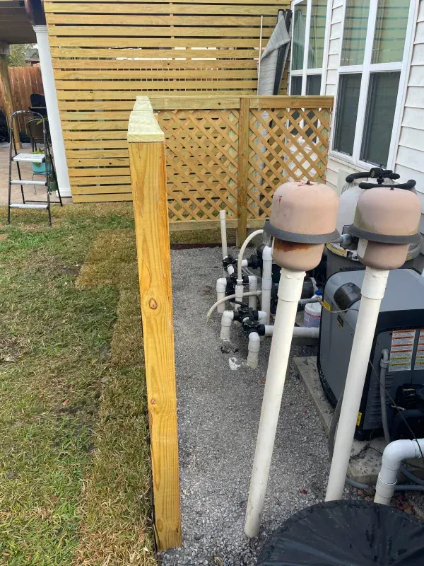 A wooden fence surrounds a swimming pool with a ladder in the background.