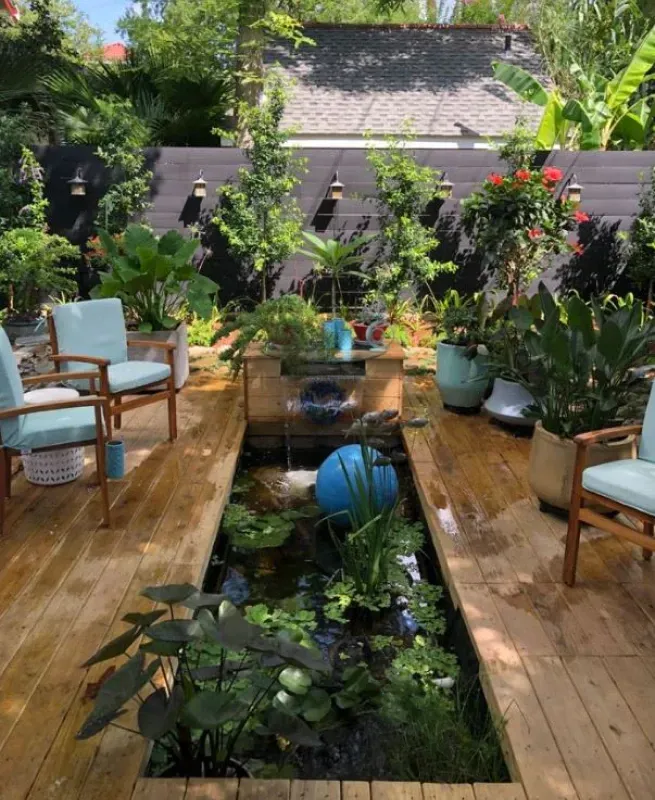 A wooden deck with a pond surrounded by plants and chairs