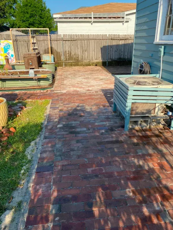 A brick walkway leading to a house in a backyard.