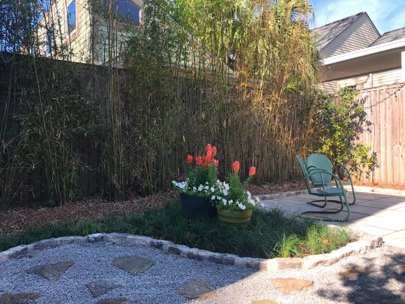 A backyard with a fence , chairs , flowers and a patio.