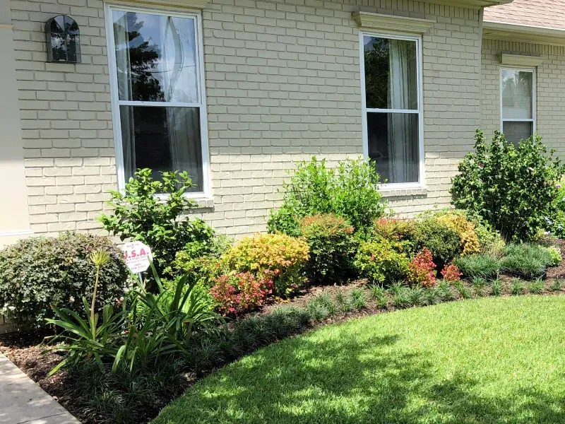 A white brick house with a lush green lawn and bushes in front of it.