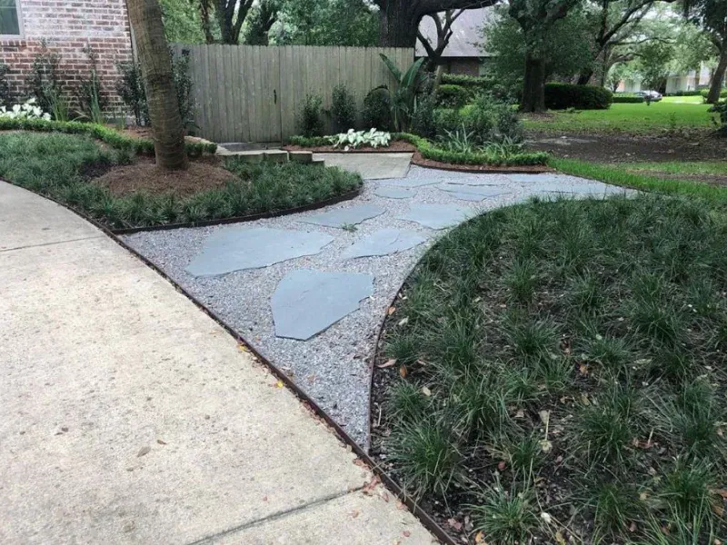 A stone walkway leading to a house with a fence in the background.