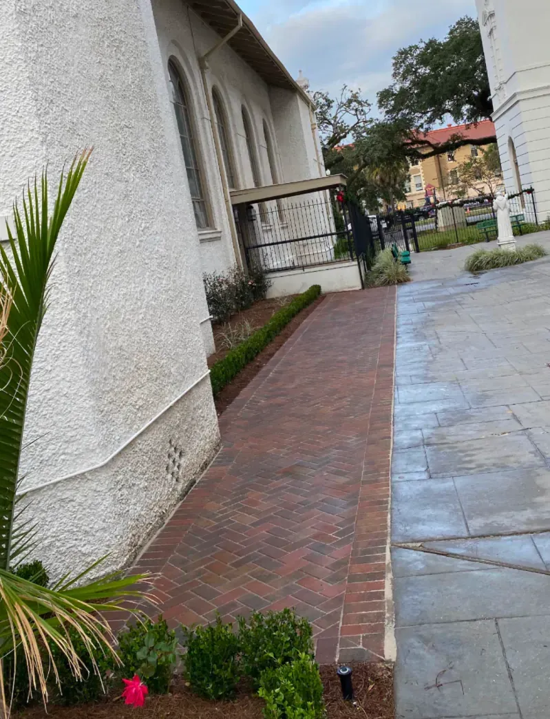 A sidewalk leading to a white building with a brick walkway