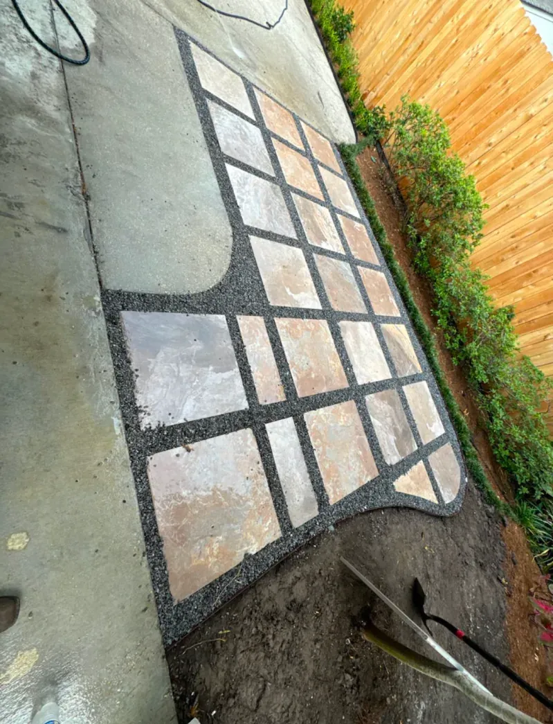 A brick walkway is being built in a backyard next to a wooden fence.