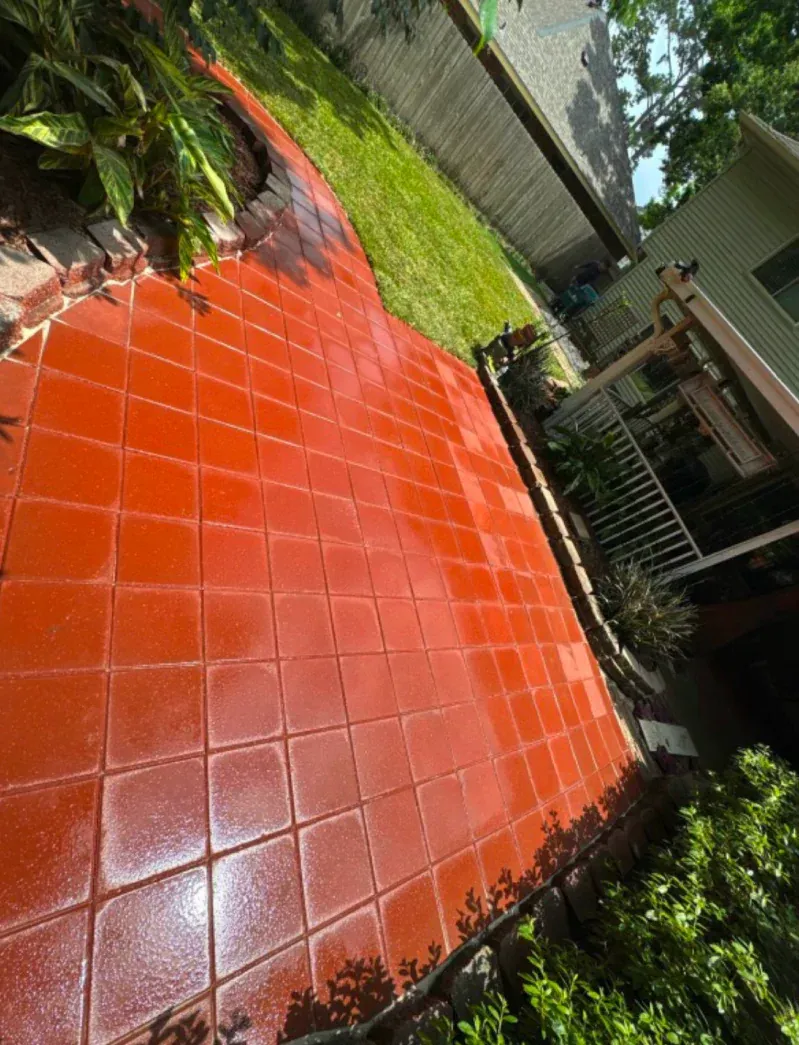 A red tiled walkway in a backyard with a house in the background.
