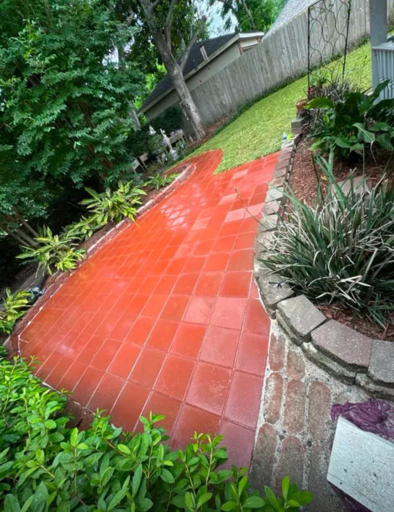 A red brick walkway in a backyard surrounded by trees and bushes.