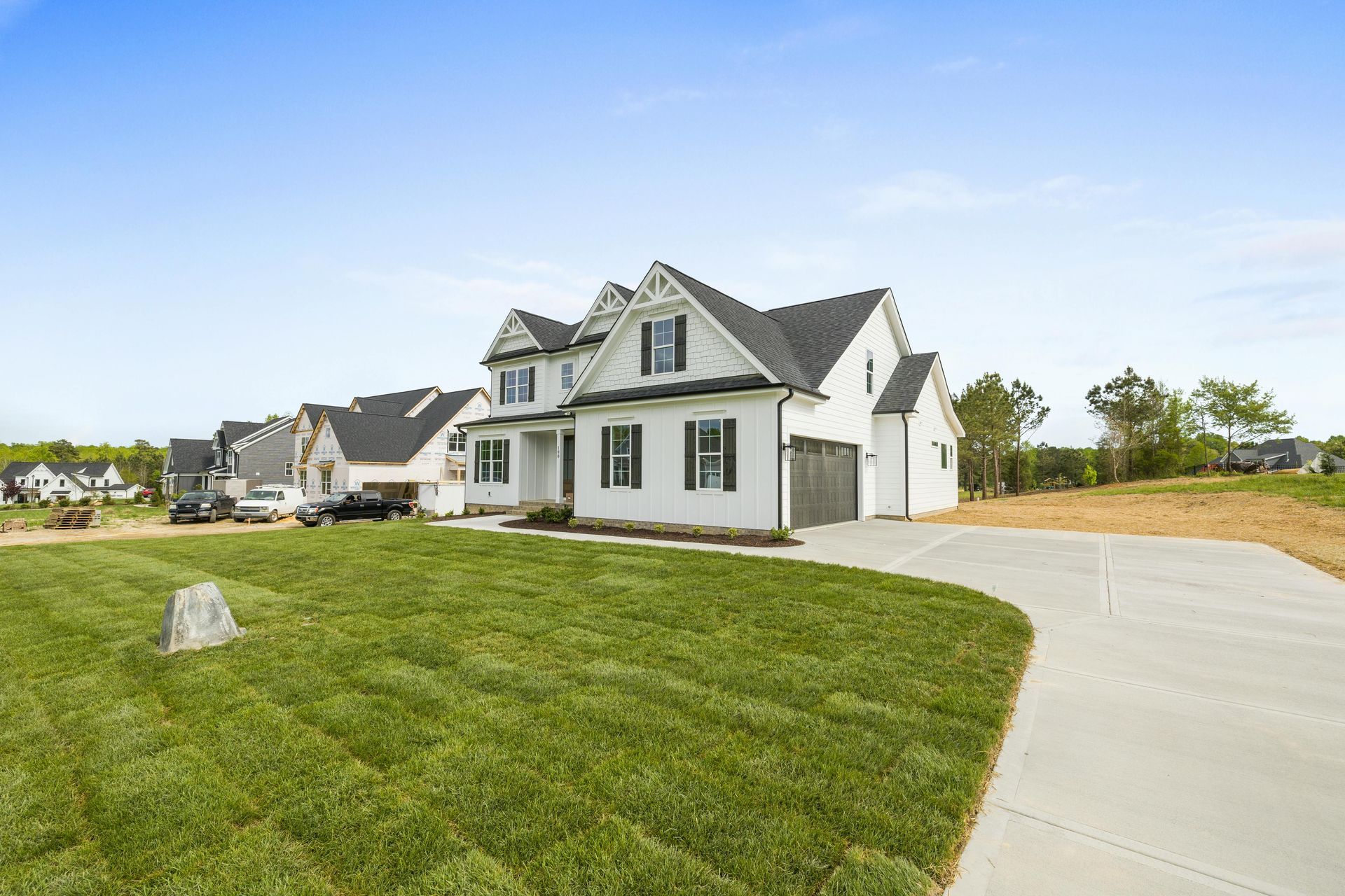 New white house with gray roof beside a curved driveway and green lawn under a clear blue sky