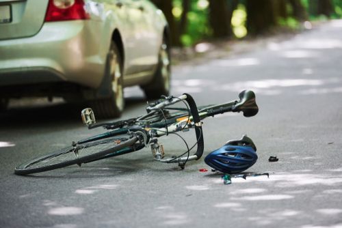 bicycle crash scene with a road bike and helmet in the road next to a car.