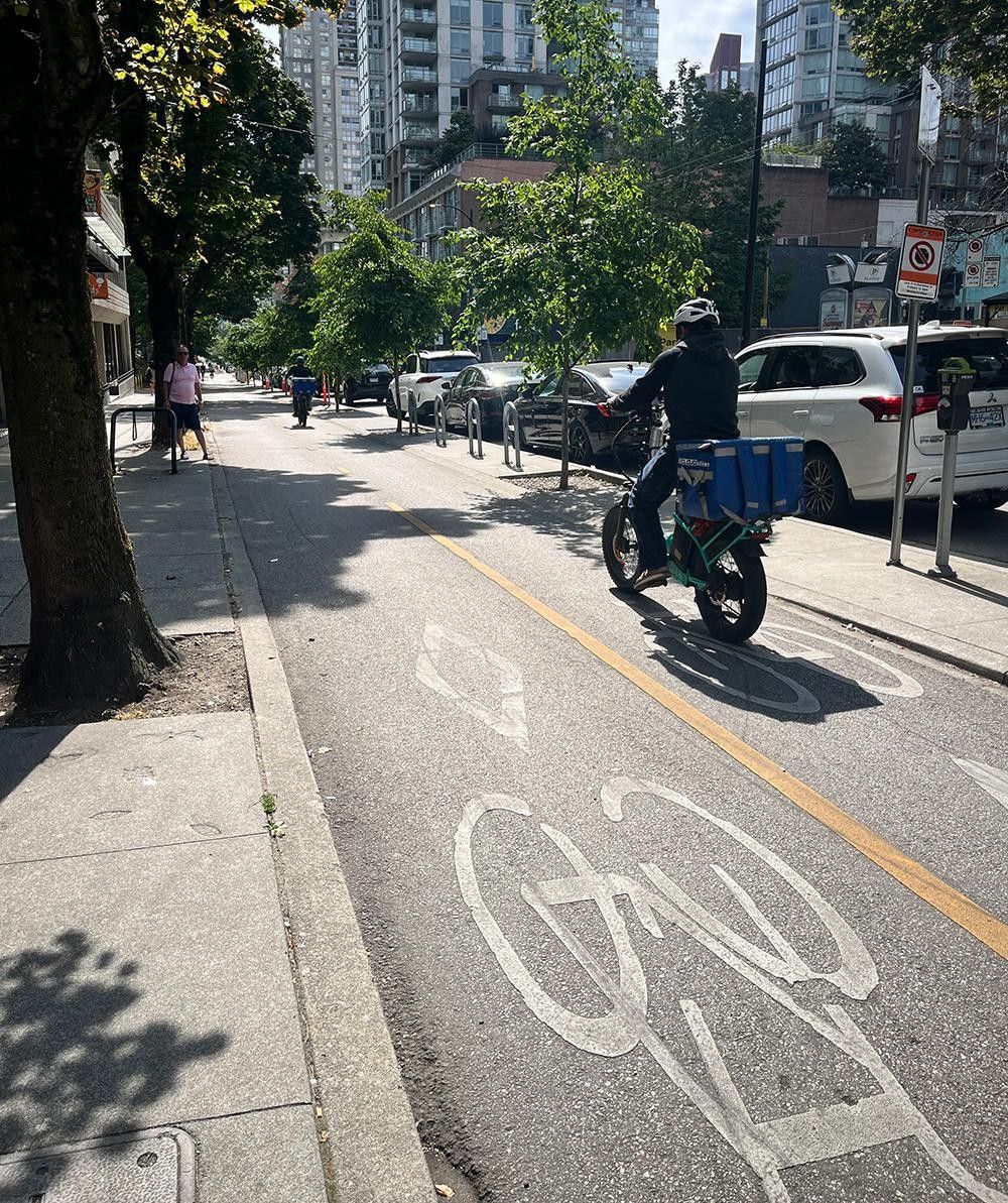 Bicycle couriers riding on a protected bicycle track in Vancouver, BC on a sunny day. Protected bike