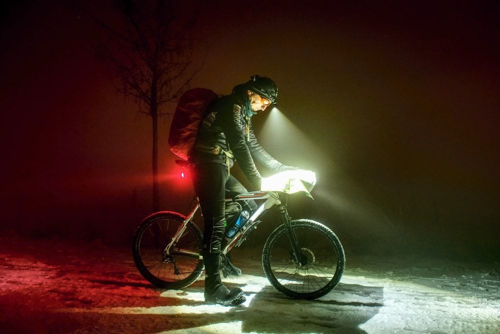 cyclist on his bike stopped at night on a snow packed road reading a map with headlamp