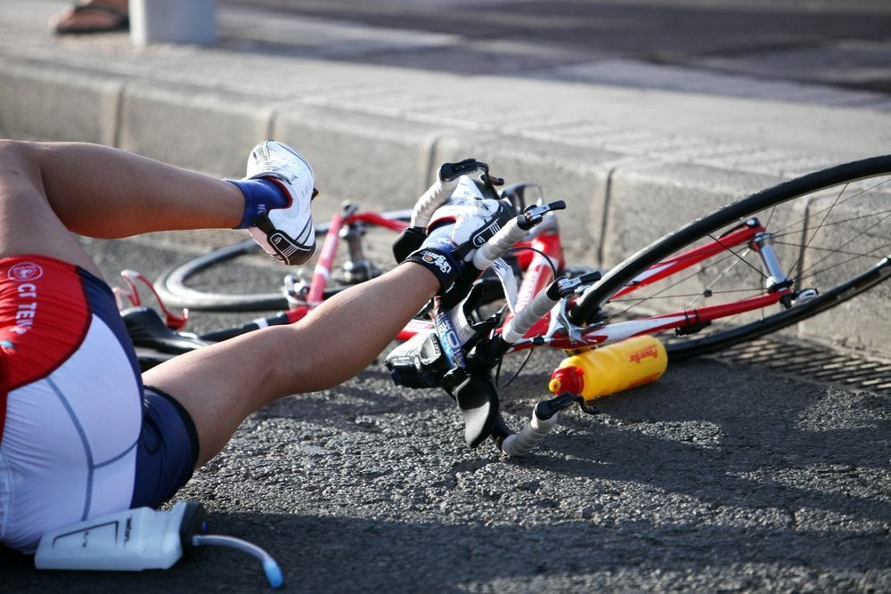 female bicyclist laying on the road next to her bicycle after a cycling crash