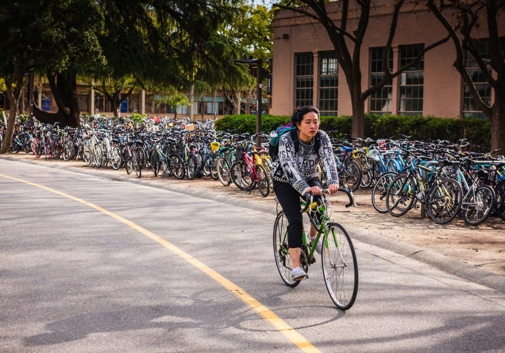 Girl biking past rows of bikes at UC Davis, the best medium-sized biking town in the U.S., 2025