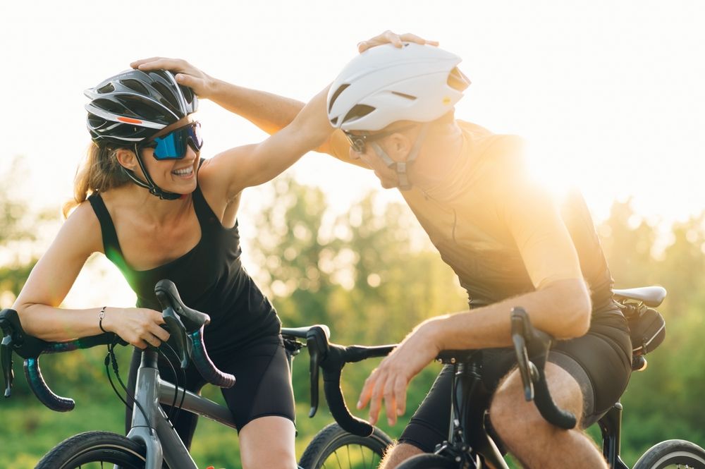Male and female bicycle riders tapping each others bicycle helmets and smiling