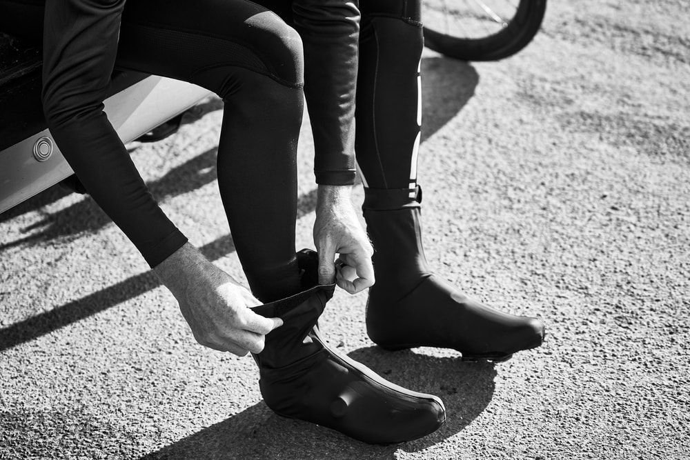 male cyclist putting on winter cycling shoes while seated, black and white image