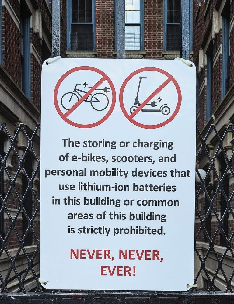 Storing scooters and e-bikes with lithium batteries is prohibited, a fire safety sign at a building entrance in Brooklyn, New York.